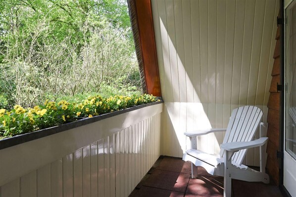 Una silla blanca en un porche con vistas a la vegetación y una ventana.
