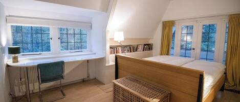 Une chambre à coucher avec un lit, un bureau, une chaise, un radiateur et une fenêtre avec des rideaux.