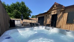 Ett bubbelbad i en trädgård, med ett trädäck, ett bord och stolar.