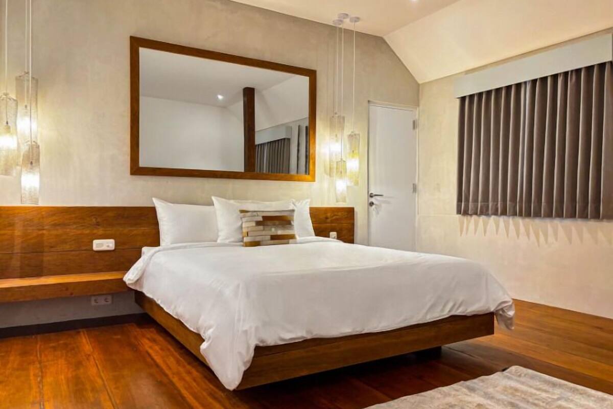 Camera da letto moderna con struttura letto in legno, biancheria da letto bianca, un ampio specchio e una finestra con tende.