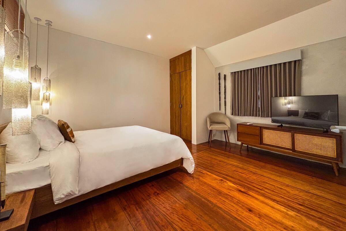 Una camera d'hotel moderna con un letto grande, una TV su un mobile in legno, una scrivania e una sedia.