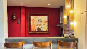 Eine Bar mit drei hölzernen Barhocker, einer roten Wand mit einem gerahmten Kunstwerk und einer Pendelleuchte.