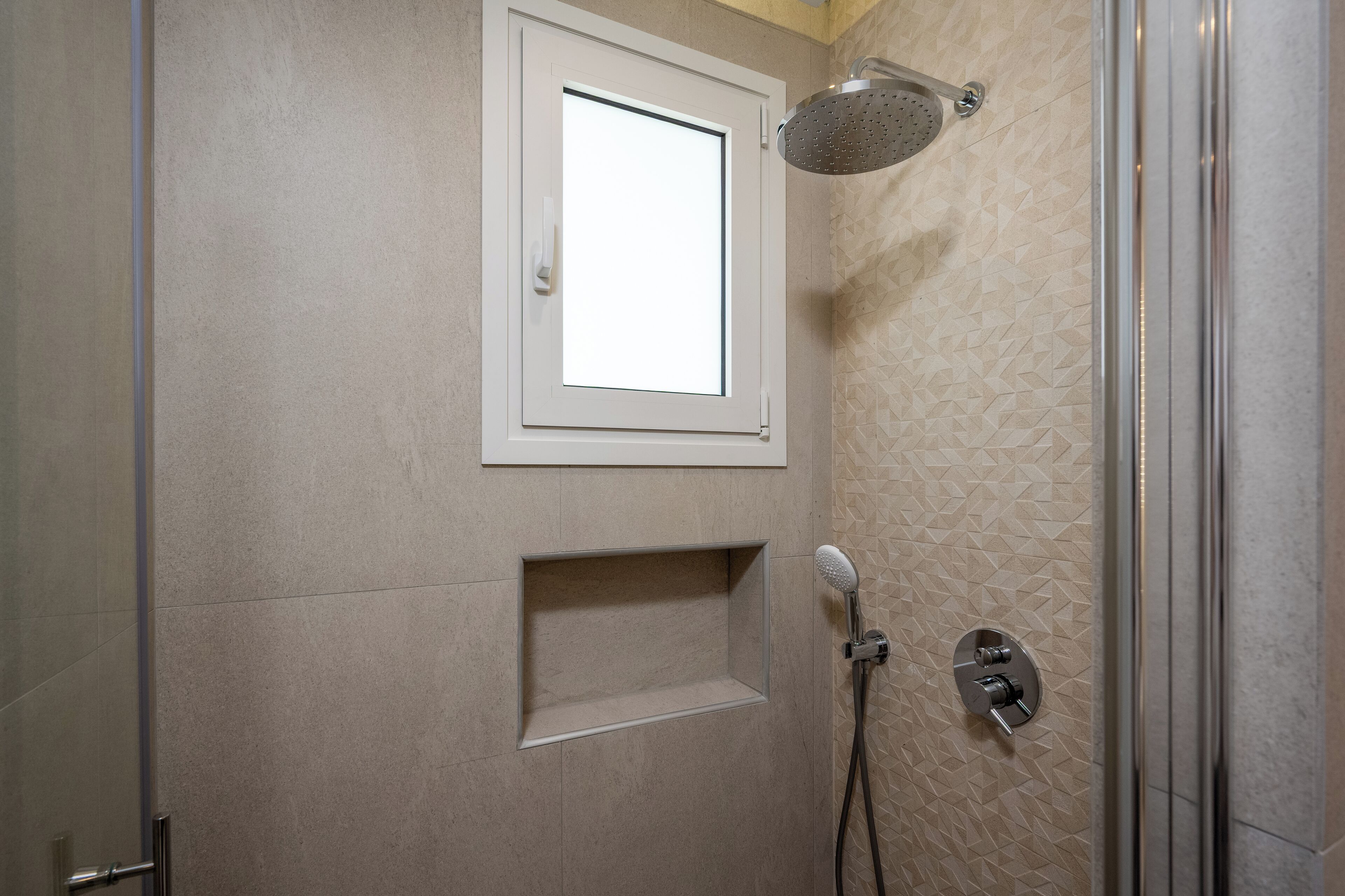 Dusche mit Handbrause, einer fest installierten Bedienfeld und einem kleinen Fenster darüber.