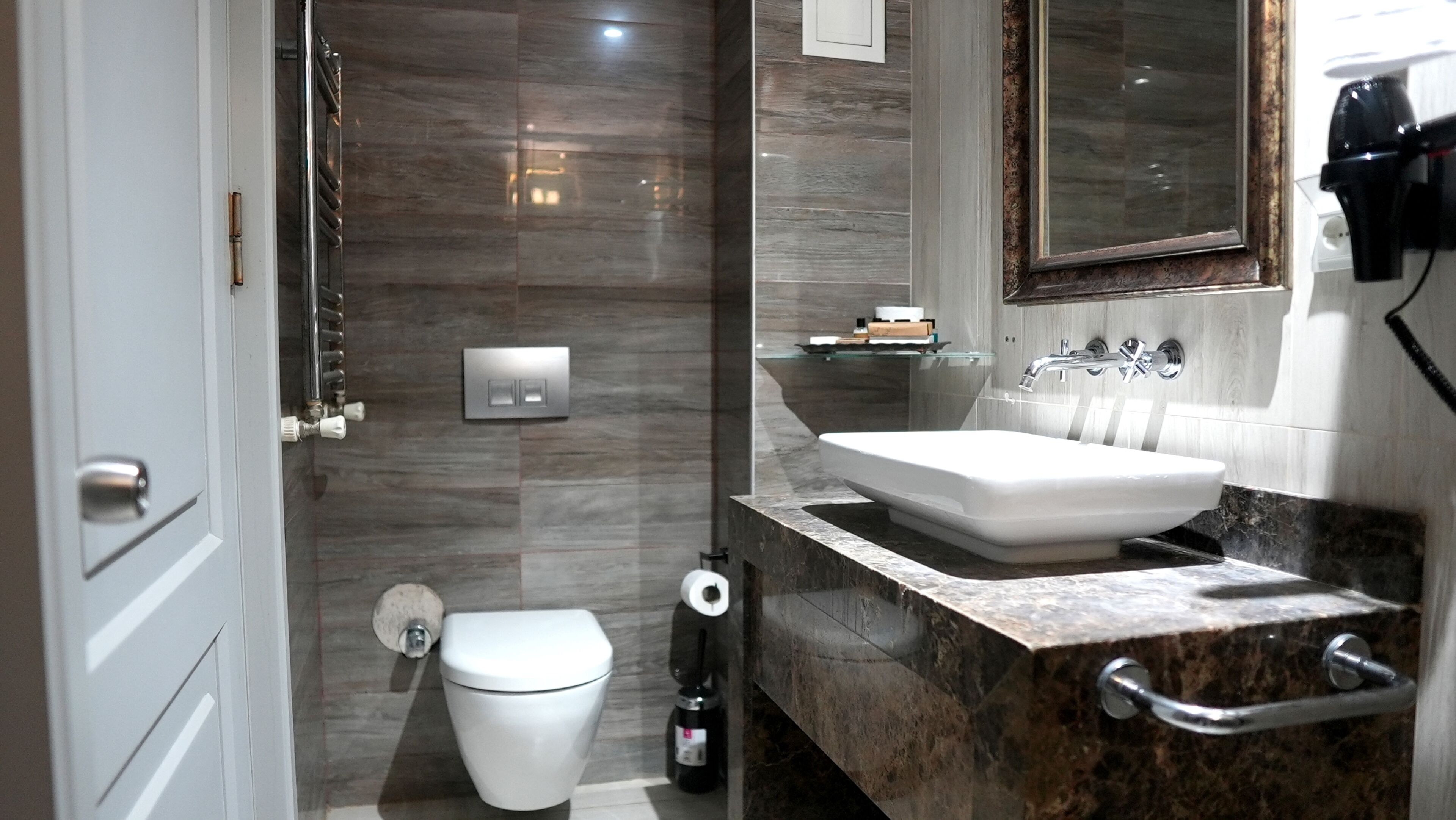 Un baño moderno con inodoro blanco, lavabo con encimera de mármol y espejo sobre el lavabo.