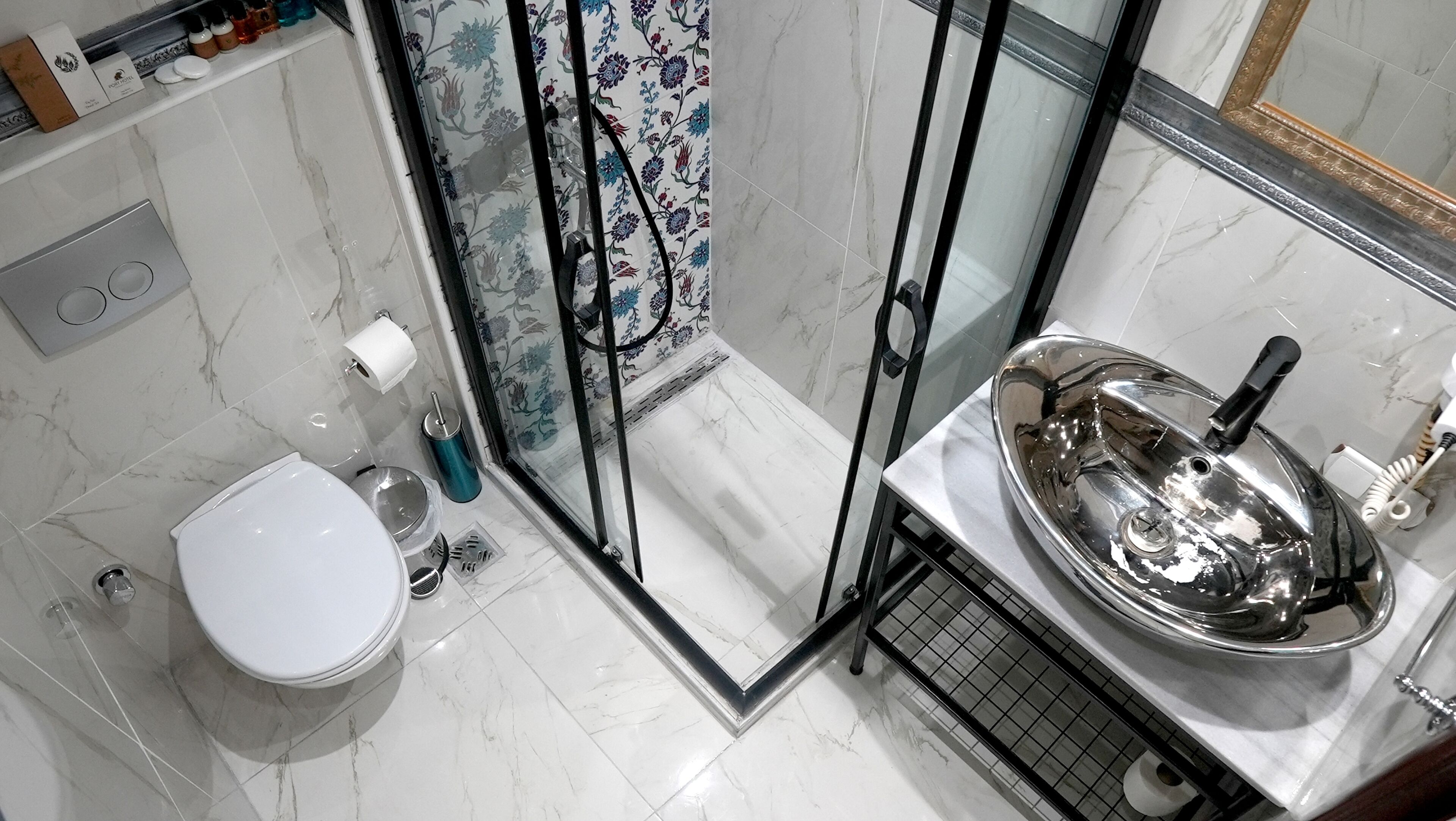 Un baño con inodoro, ducha con puerta de cristal y lavamanos de acero inoxidable.