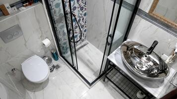 Un baño con inodoro, ducha con puerta de cristal y lavamanos de acero inoxidable.