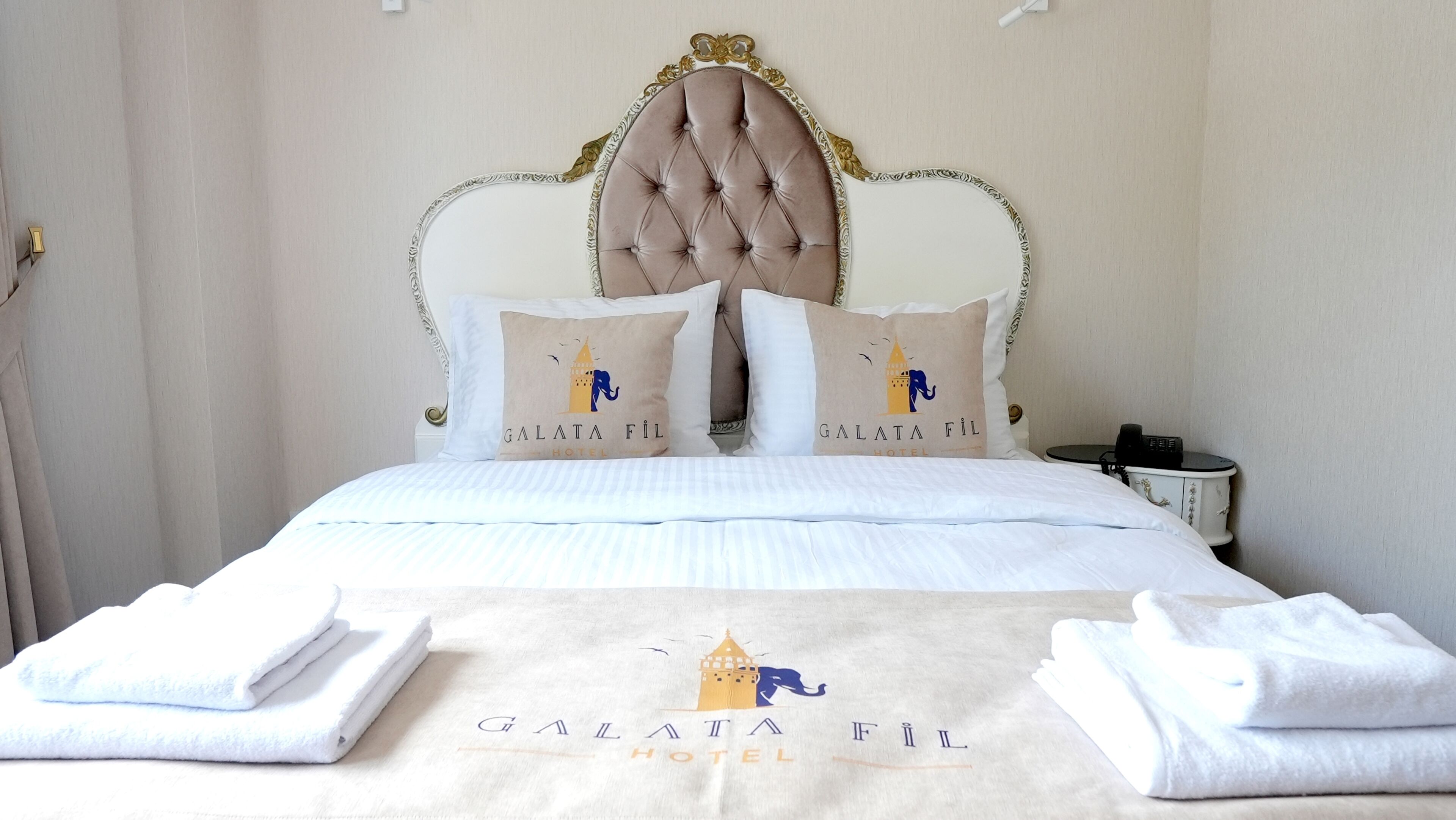 A hotel room with a bed, pillows, a bedside table, and a wall-mounted phone.