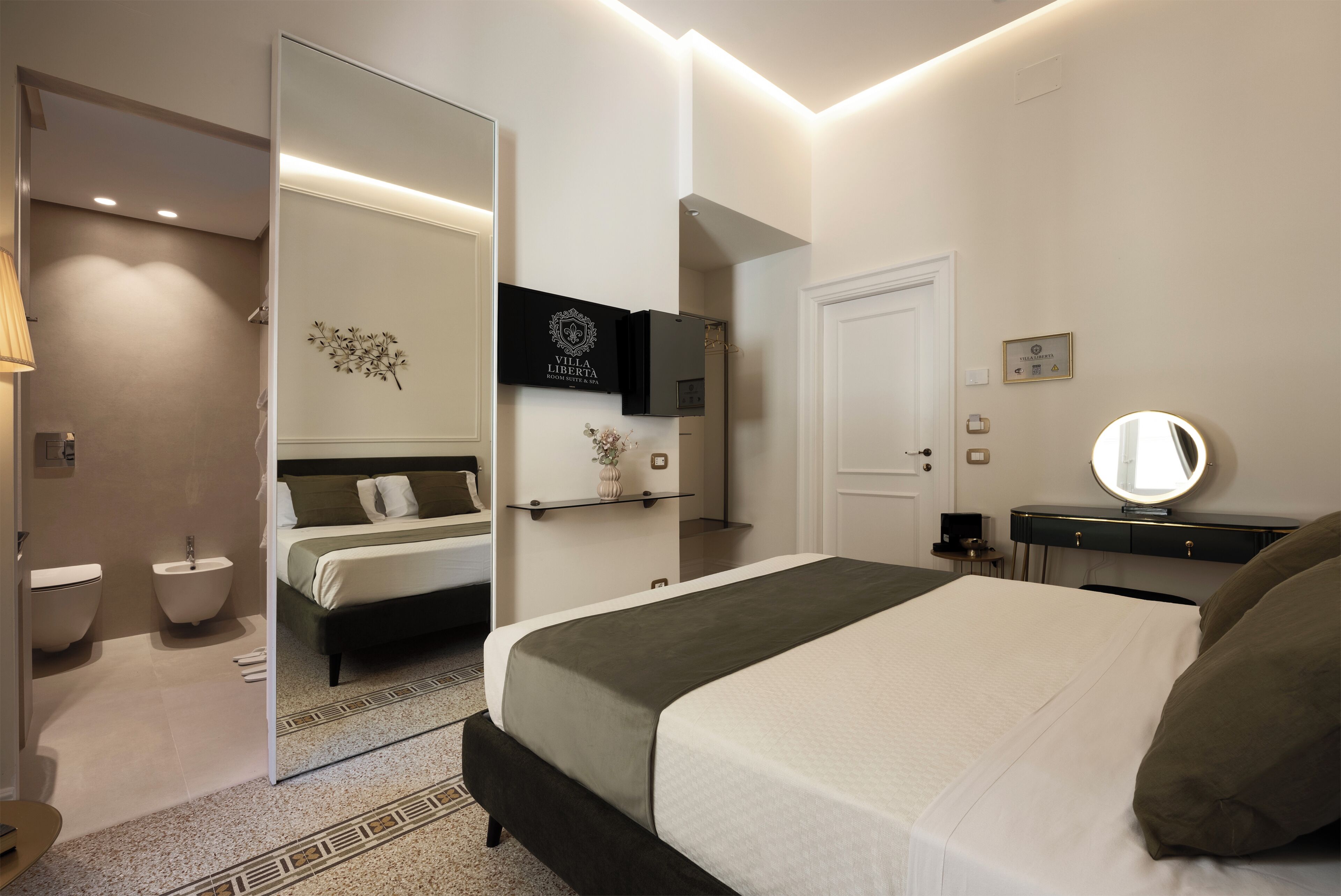 Una habitación de hotel moderna con una cama grande, mesita de noche, espejo y televisor montado en la pared.