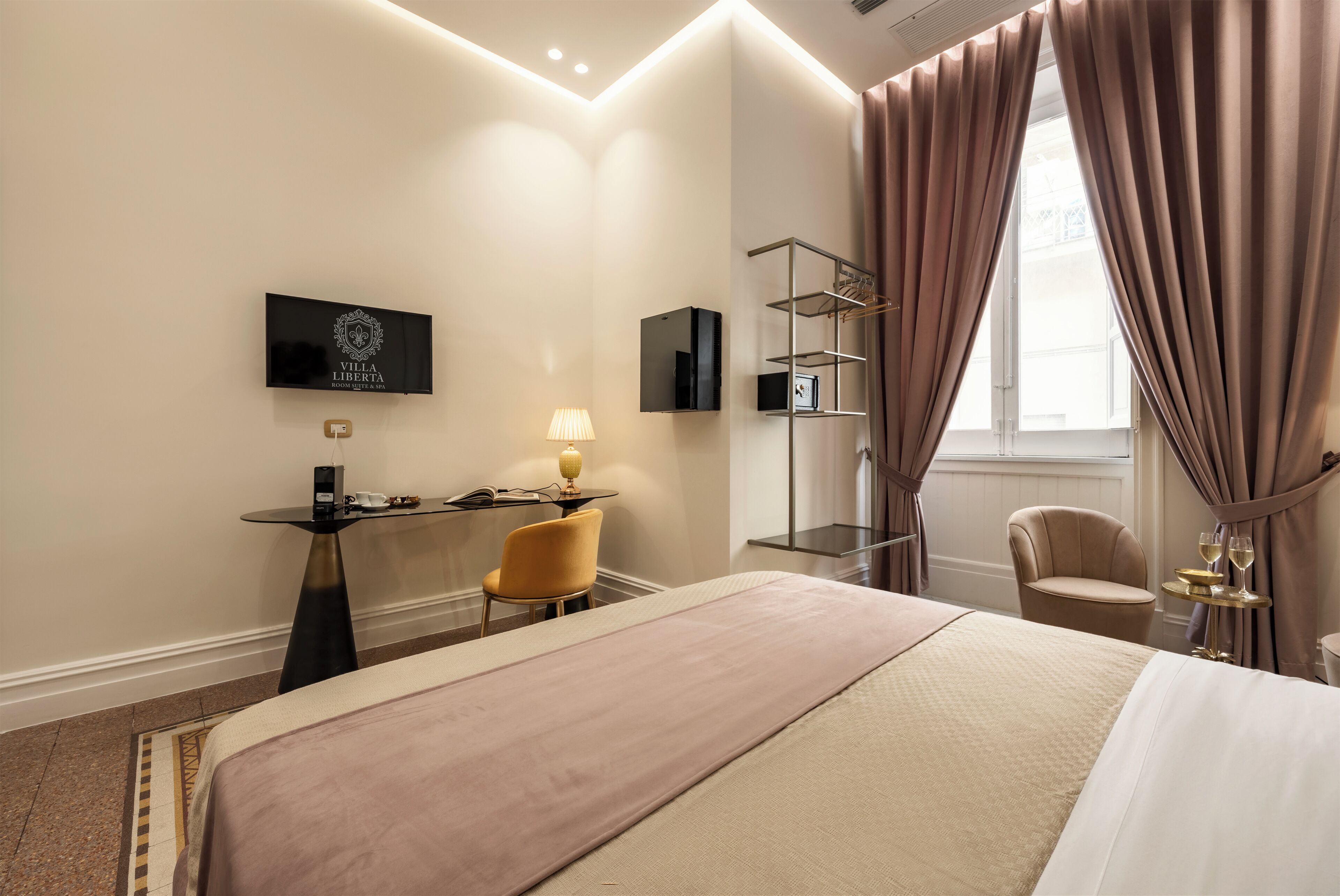 Une chambre d’hôtel avec un lit, un bureau avec une lampe, une chaise, un téléviseur et une fenêtre avec des rideaux.