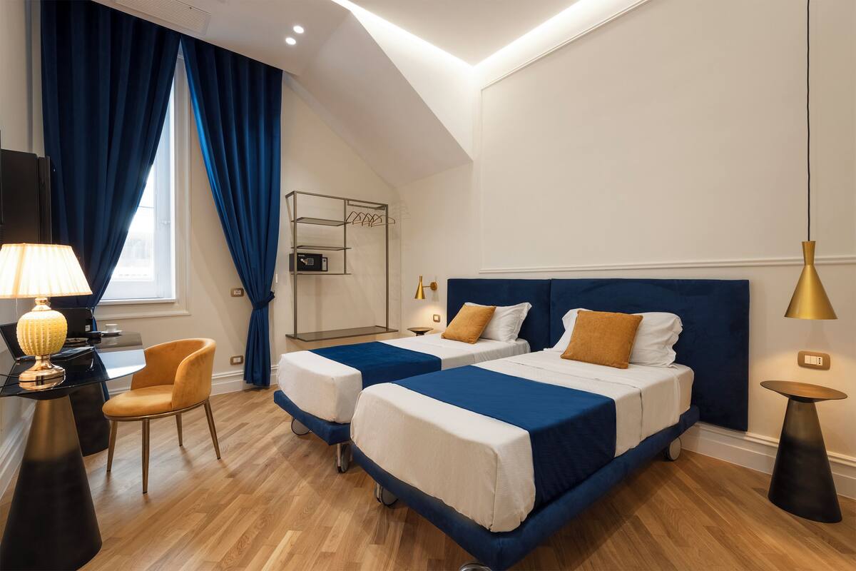 A hotel room with two beds, a desk with a lamp, a chair, and a small table.