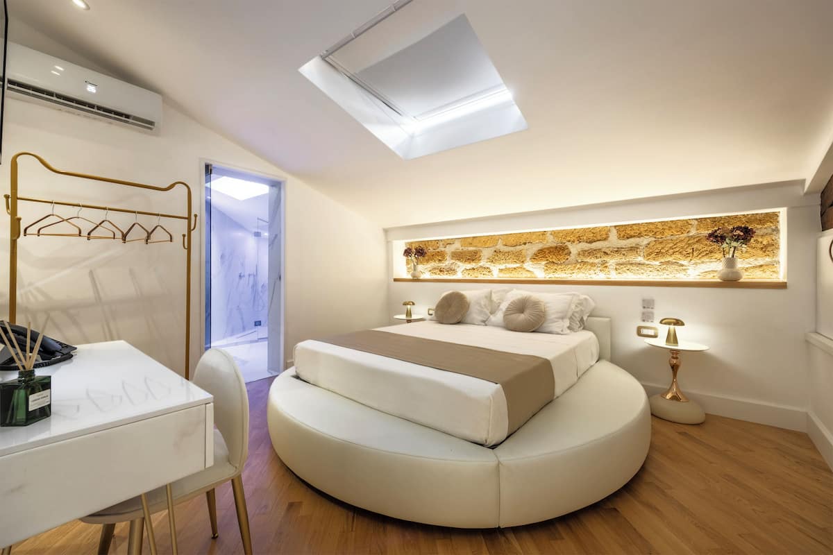 A modern bedroom with a skylight, a bed with a headboard, a bedside table, and a wall-mounted shelf.