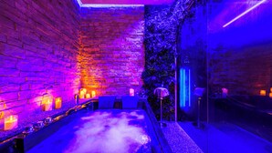 Een wellnessruimte met een stenen muur, kaarsen en een jacuzzi.