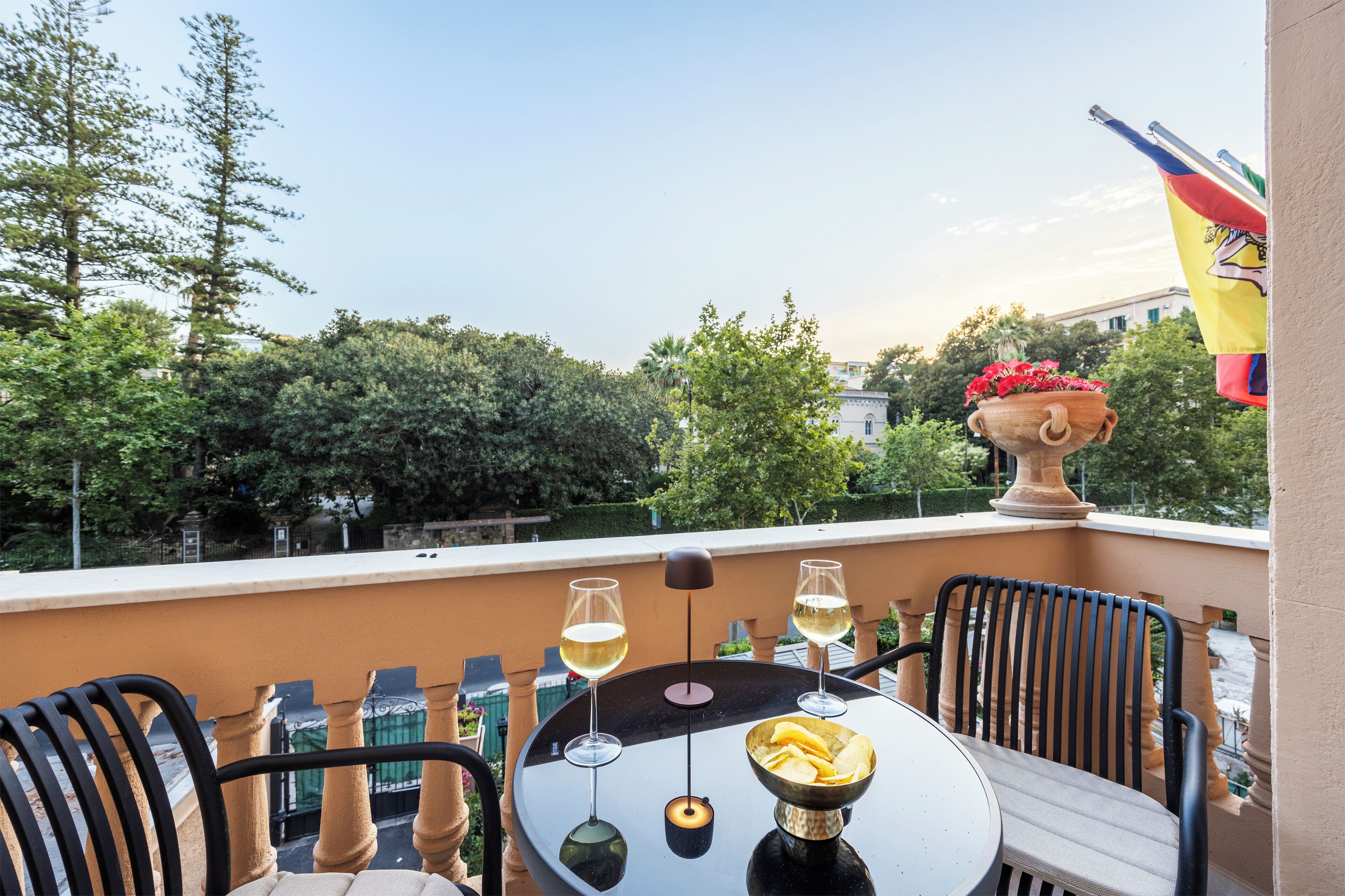 Ein Balkon mit Tisch, zwei Stühlen, einer Schale mit Snacks und zwei Gläsern Weißwein.