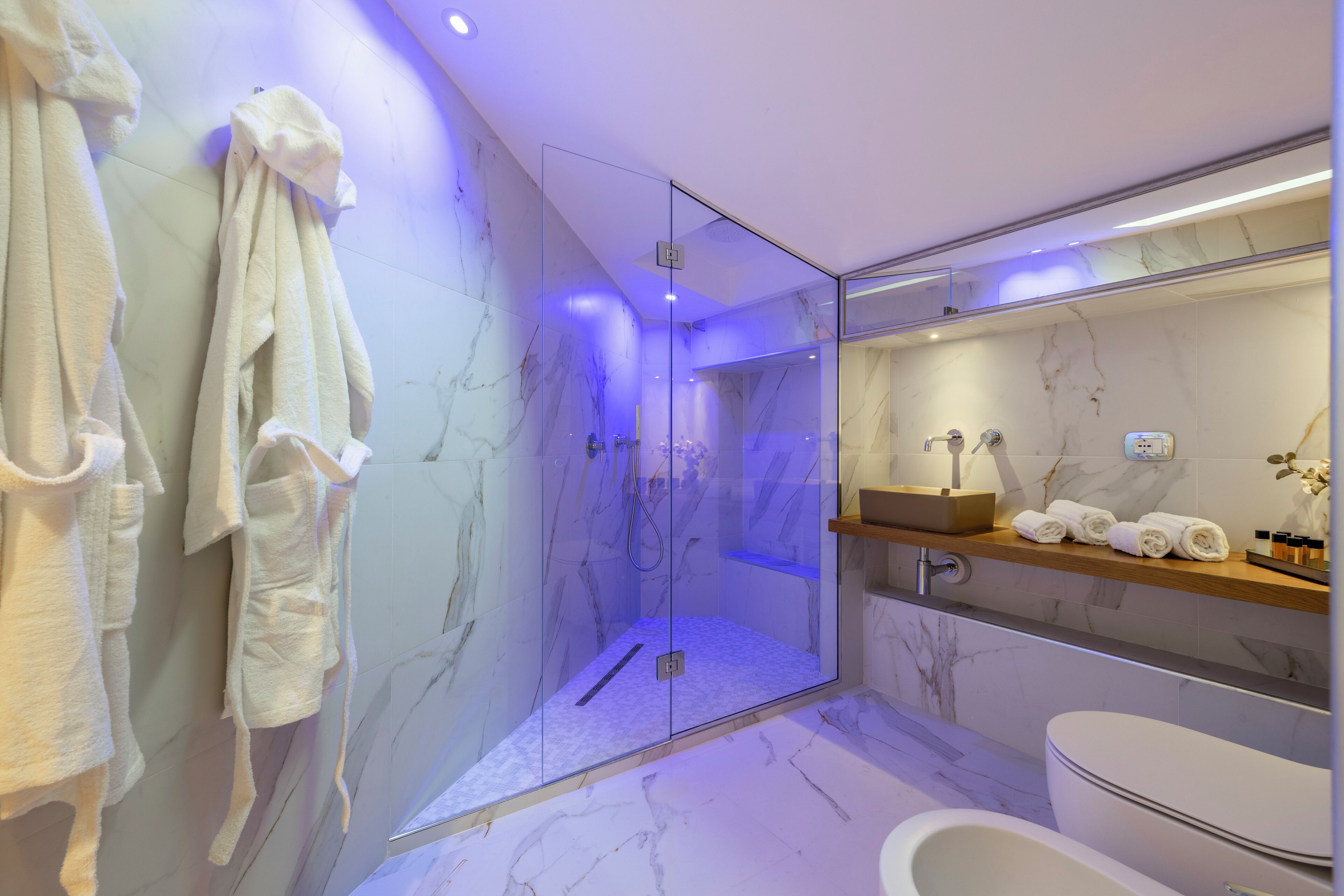 A modern bathroom with a glass-enclosed shower, marble walls, and a vanity with towels.