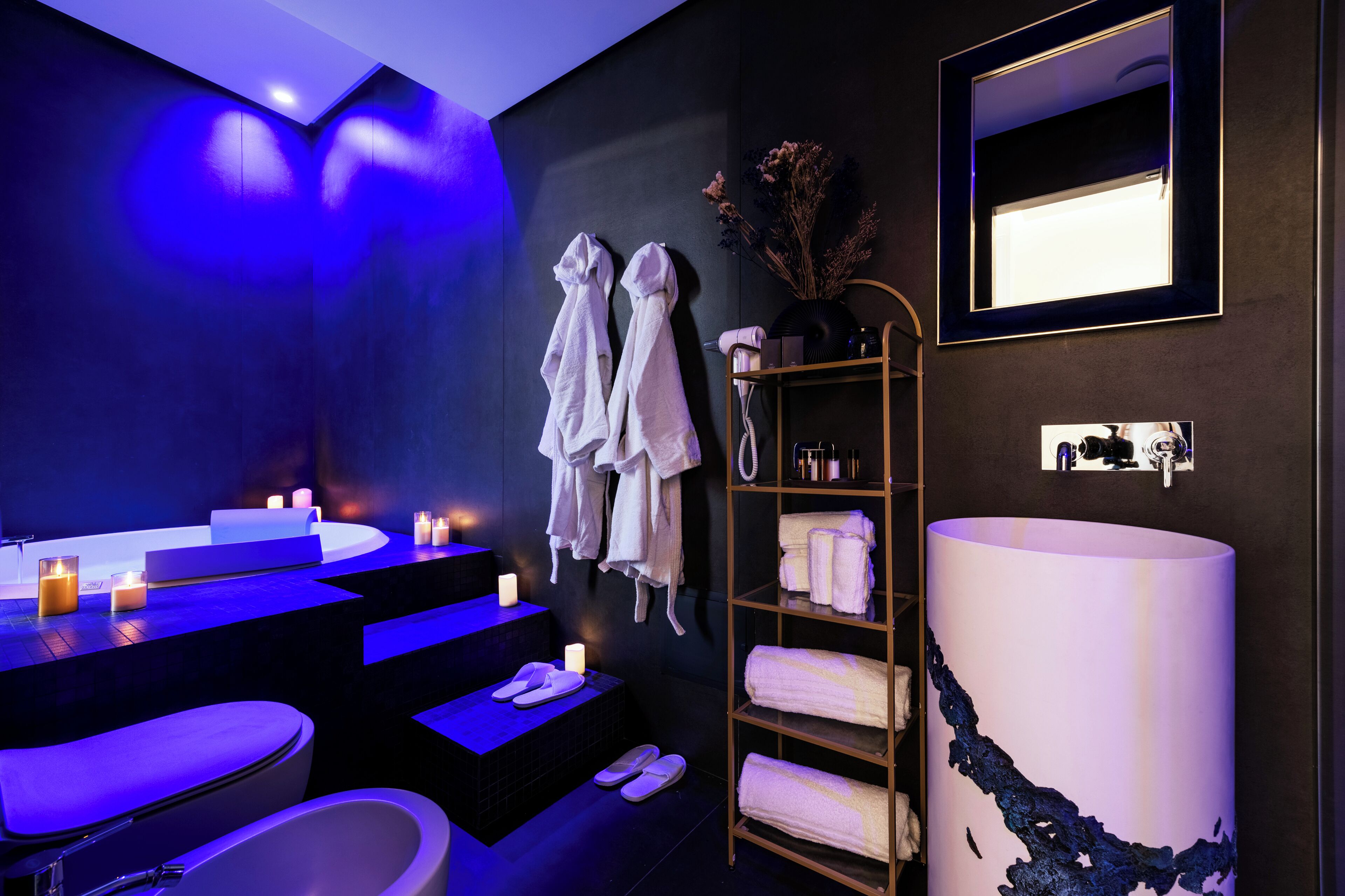 A modern bathroom with a large bathtub, a sink, and a shower. There are towels and toiletries on shelves.