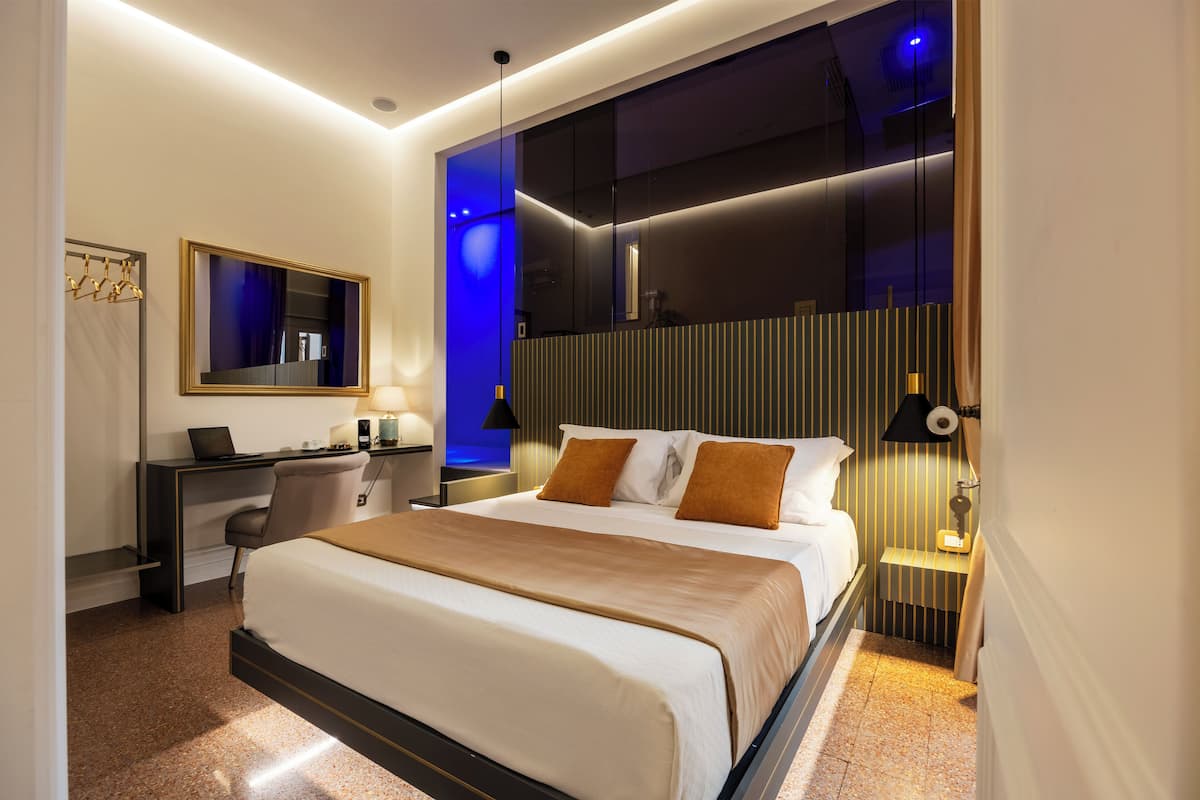 A modern hotel room with a large bed, a desk with a laptop, and a mirror.