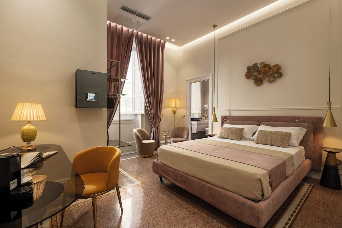 A hotel room with a large bed, a desk with a lamp, a chair, and a television.