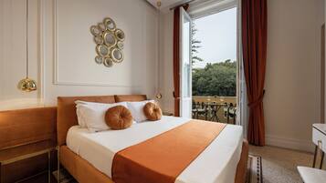 A hotel room with a large bed, a desk, and a balcony with a view of trees.