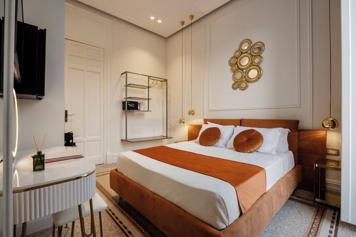 A modern hotel room with a large bed, a desk with a chair, a wardrobe, and a TV mounted on the wall.