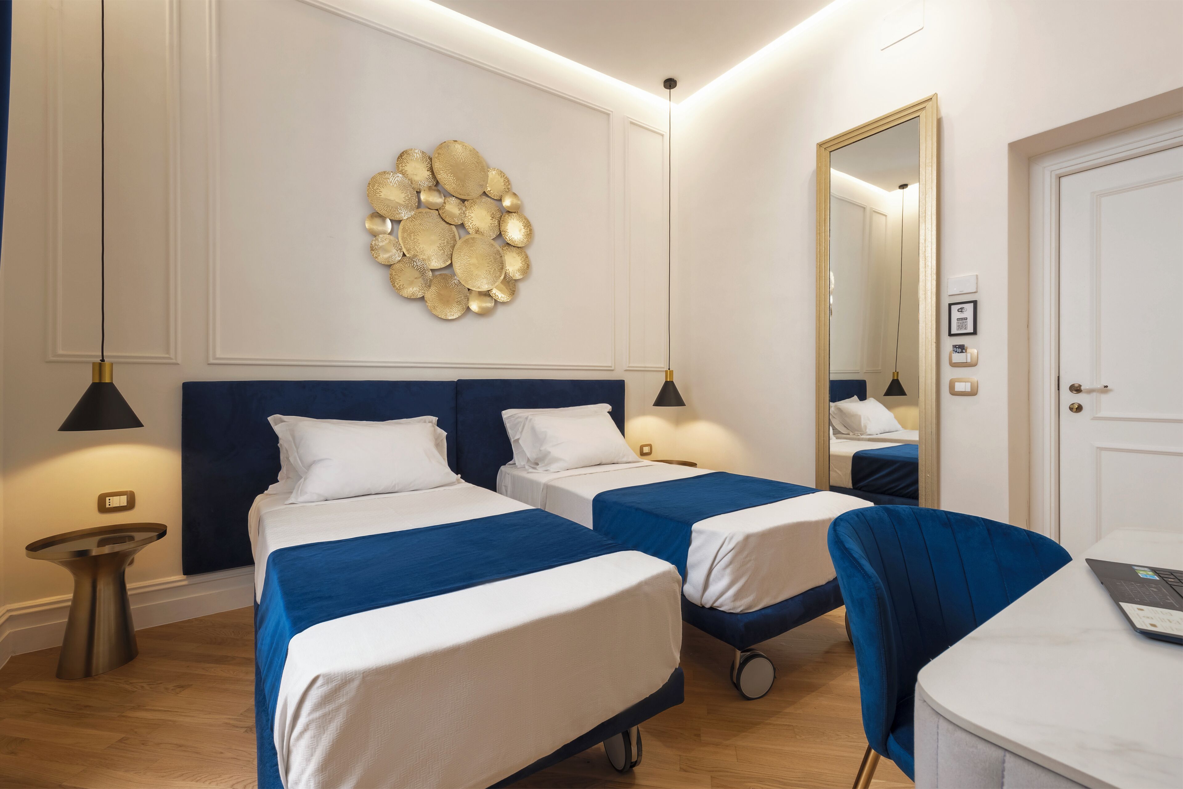 A hotel room with two beds, a desk, a chair, a wall-mounted decorative piece, and a mirror.