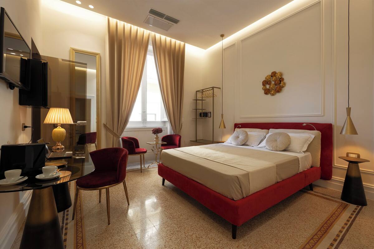 A hotel room with a large bed, a desk with a computer, a chair, a TV, and a window with curtains.