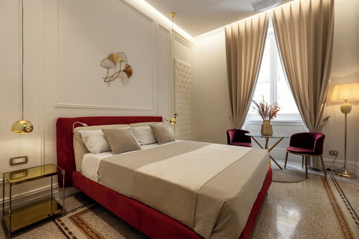 A hotel room with a large bed, a small table, two chairs, a lamp, and a decorative wall piece.
