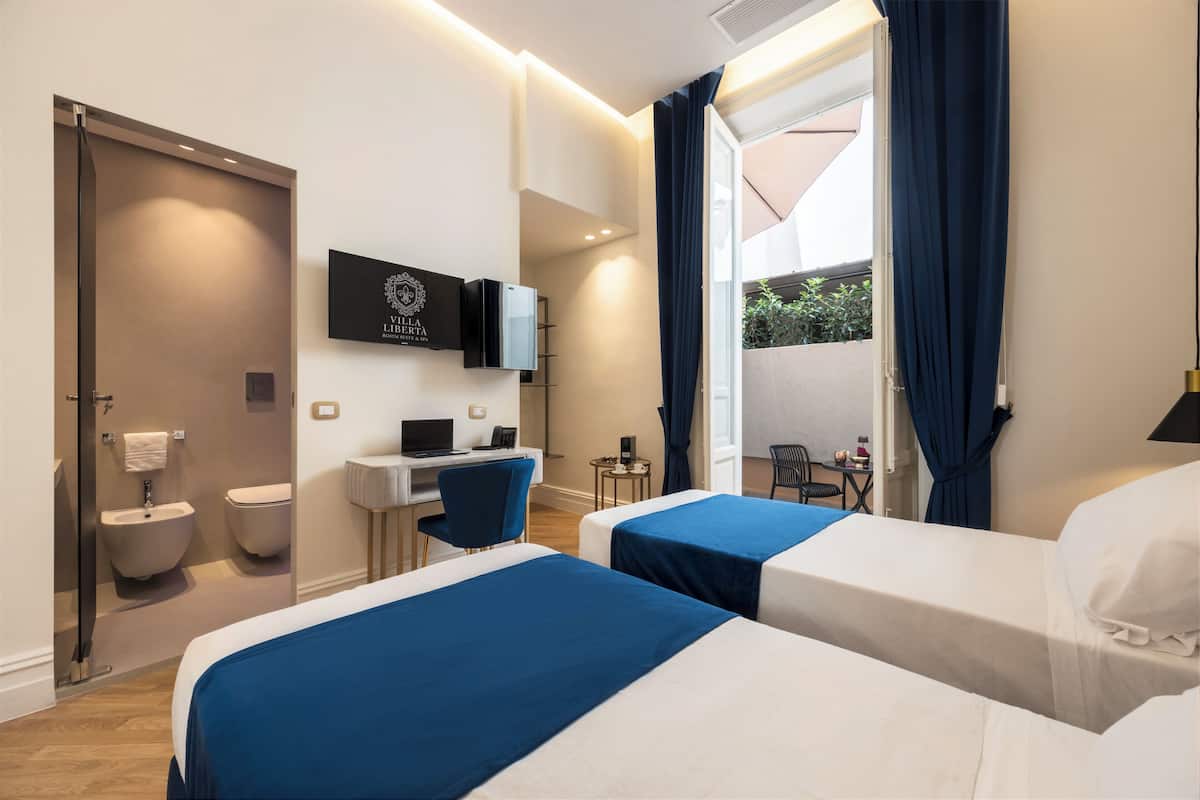 A hotel room with two beds, a desk, a TV, and a view of the outside.
