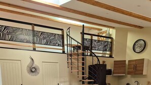 A modern kitchen with wooden cabinets, a black spiral staircase, and a dining area with a wooden table and white chairs.