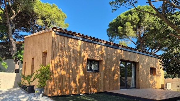 A modern wooden cabin with a tiled roof, a small deck, and a paved patio area.