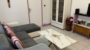 A living room with a grey sectional sofa, a small grey ottoman, a marble coffee table, and a cabinet with glass doors. - Urban Shelter (Sarvelles)