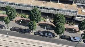 An aerial view of a parking lot with several cars parked, surrounded by trees and a modern building with a flat roof. - Urban Shelter (Sarvelles)