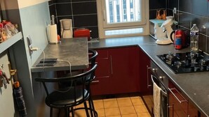 A compact kitchen with a black countertop, red cabinets, a coffee maker, and a stove. - Urban Shelter (Sarvelles)