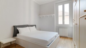 A bedroom with a bed, a bedside table, a window, and a radiator. - GuestHost - Milan City Studies Balcony Apt (Milan)