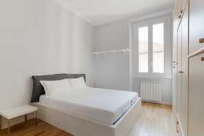 A bedroom with a bed, a bedside table, a window, and a radiator.