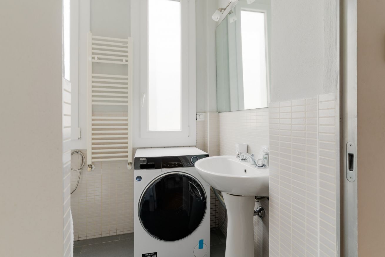 A compact bathroom with a washing machine, a sink, and a mirror.