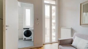 A room with a washing machine, a radiator, a sofa, and a sliding glass door leading to an outdoor balcony. - GuestHost - Milan City Studies Balcony Apt (Milan)