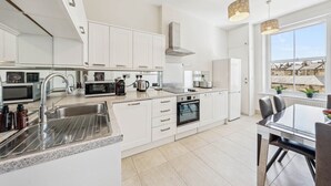 A modern kitchen with white cabinetry, stainless steel appliances, and a large window providing a view of the outside. - Stunning 3-Bedroom Apartment in Hampstead (London)