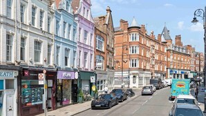 A street lined with colorful buildings, including a pharmacy and a restaurant. - Stunning 3-Bedroom Apartment in Hampstead (London)