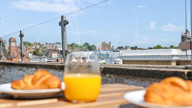 A breakfast table with croissants and orange juice, overlooking a cityscape with buildings and a clock tower. - Stunning 3-Bedroom Apartment in Hampstead (London)