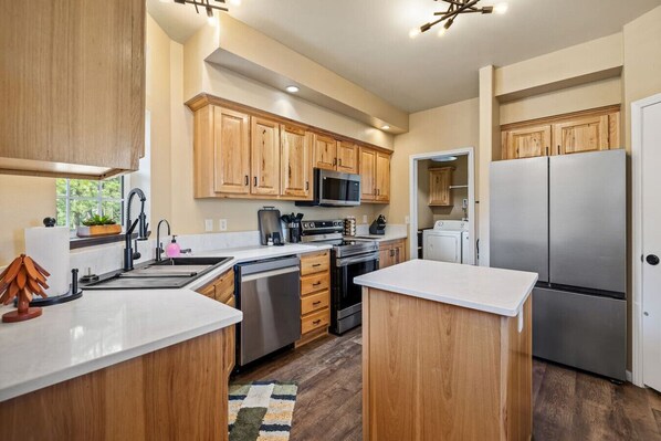 A modern kitchen with wooden cabinets, stainless steel appliances, and a white countertop.