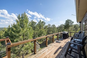 A wooden deck with outdoor seating and a view of a forest.