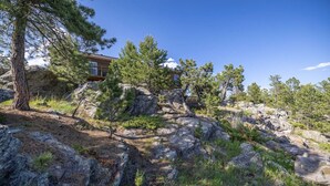 Une cabane aux murs en pierre, entourée d’un paysage rocheux et de pins.
