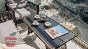 Un balcón alto con mobiliario de mimbre, una mesa de vidrio con tazas de té y una revista Louis Vuitton.