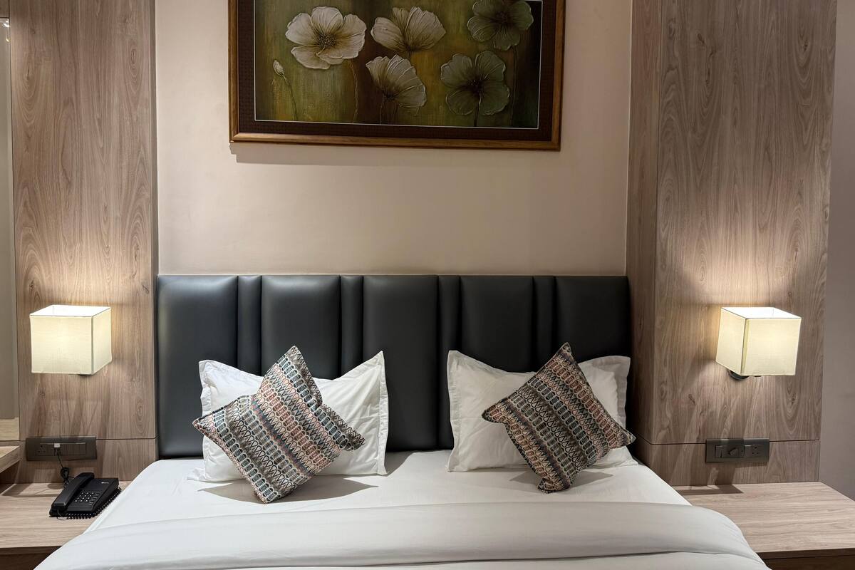 A hotel room with a bed, two patterned pillows, a headboard, bedside lamps, a painting, and a telephone on the nightstand.
