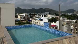 A rooftop pool with a view of a cityscape and mountains in the background. - Hotel Acksia Inn (Udaipur)