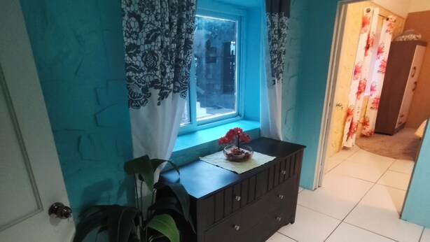A room with a window, a dresser, a potted plant, and a door. - 2-bedroom apartment in lovely Sunny Acres with WiFi, AC and Fan (Choc)