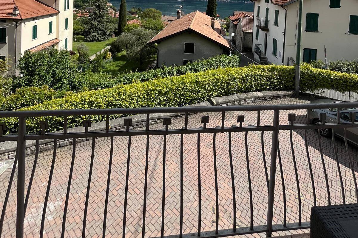 Une vue pittoresque d’un village au bord d’un lac, avec ses bâtiments traditionnels, une promenade dallée et des montagnes en arrière-plan.