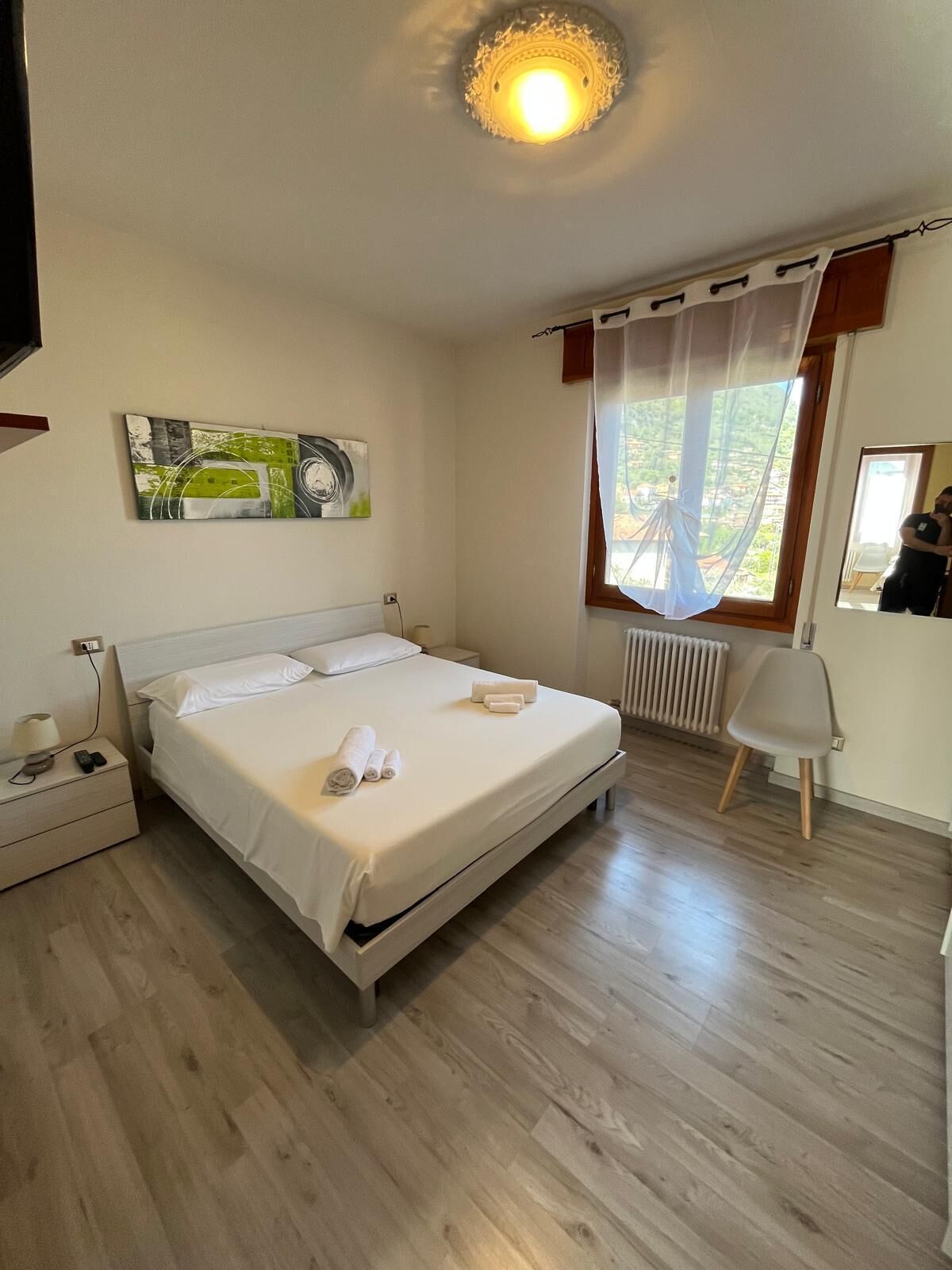 Una camera da letto con un letto, un comodino, una sedia, un termosifone e una finestra con tende.
