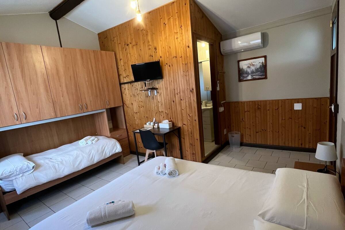 Une chambre d’hôtel avec un grand lit, deux petits lits, un bureau et un téléviseur fixé au mur.
