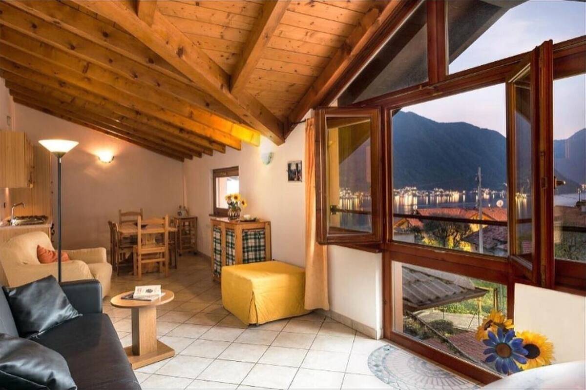Un salon chaleureux avec un plafond en bois, un canapé, une table à manger et une vue sur les montagnes grâce à de grandes fenêtres.